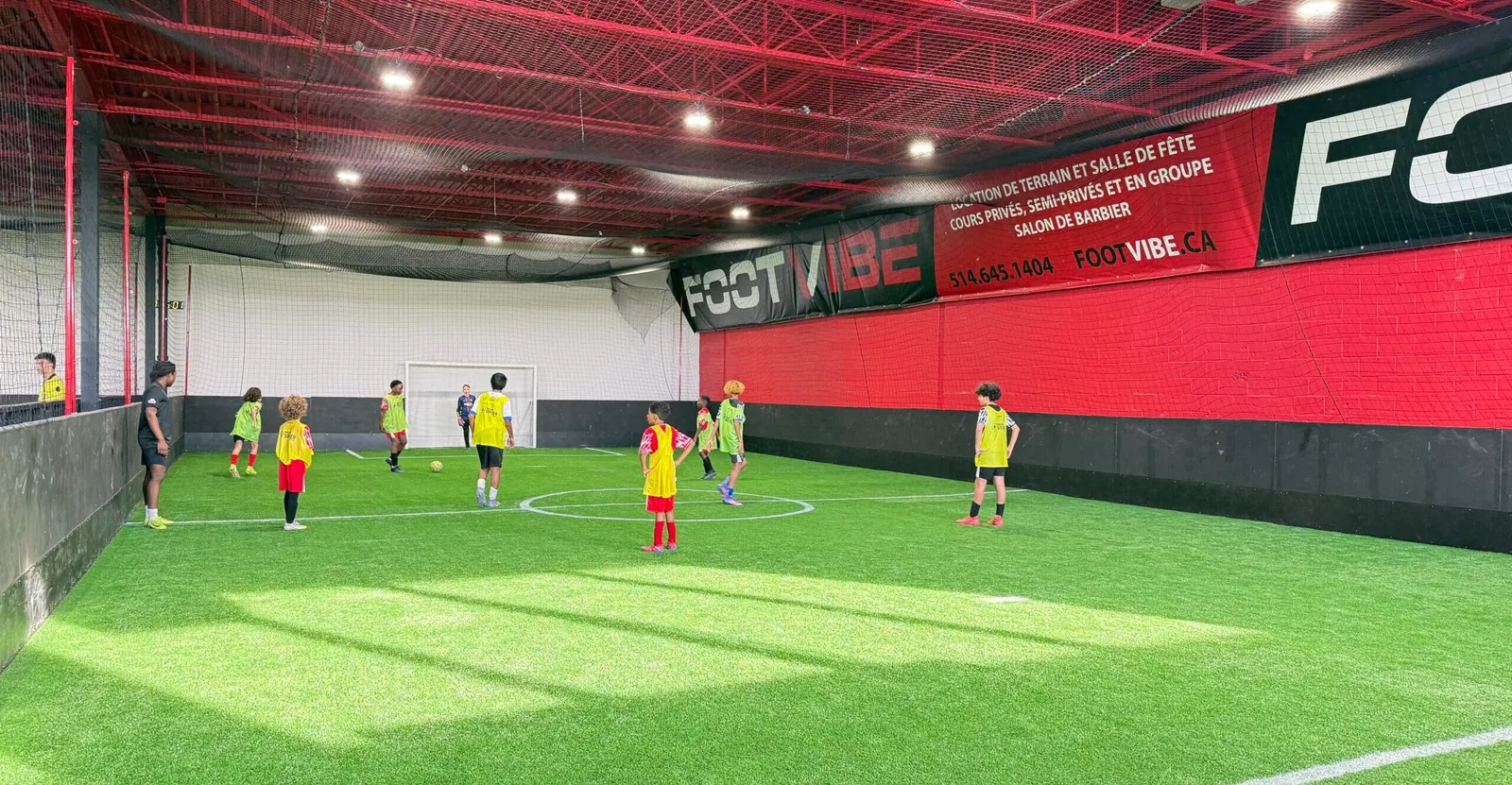 Kids in yellow and red bibs playing a game on the FootVibe indoor soccer field in Montreal East