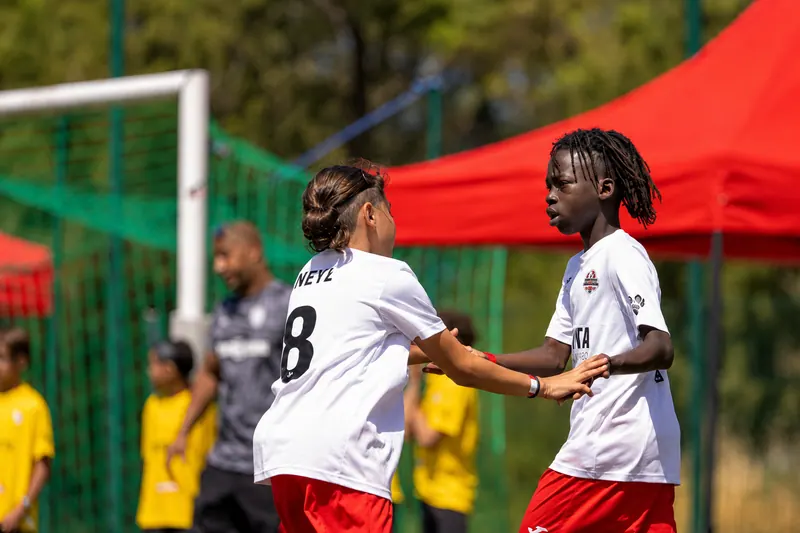 Deux joueurs de l'Académie Révolution en maillot blanc et short rouge se félicitant sur le terrain pendant un match de la Grinta Cup