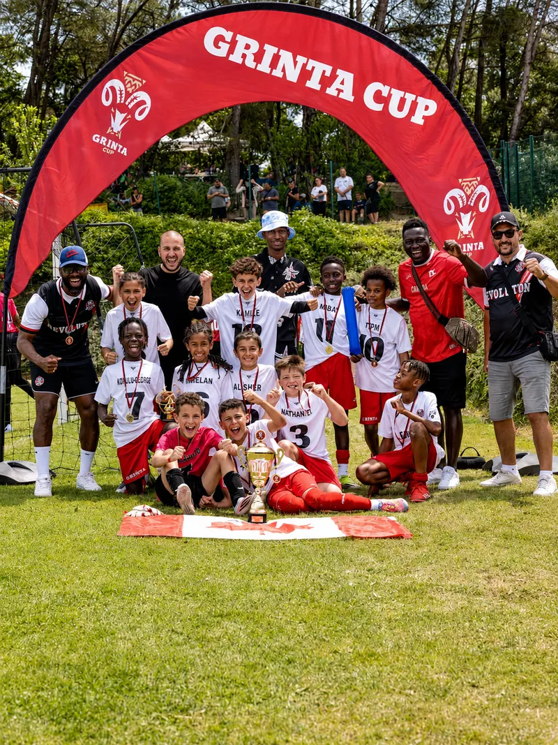 Revolution Football team with its coaches and a cup under the Grinta Cup arch