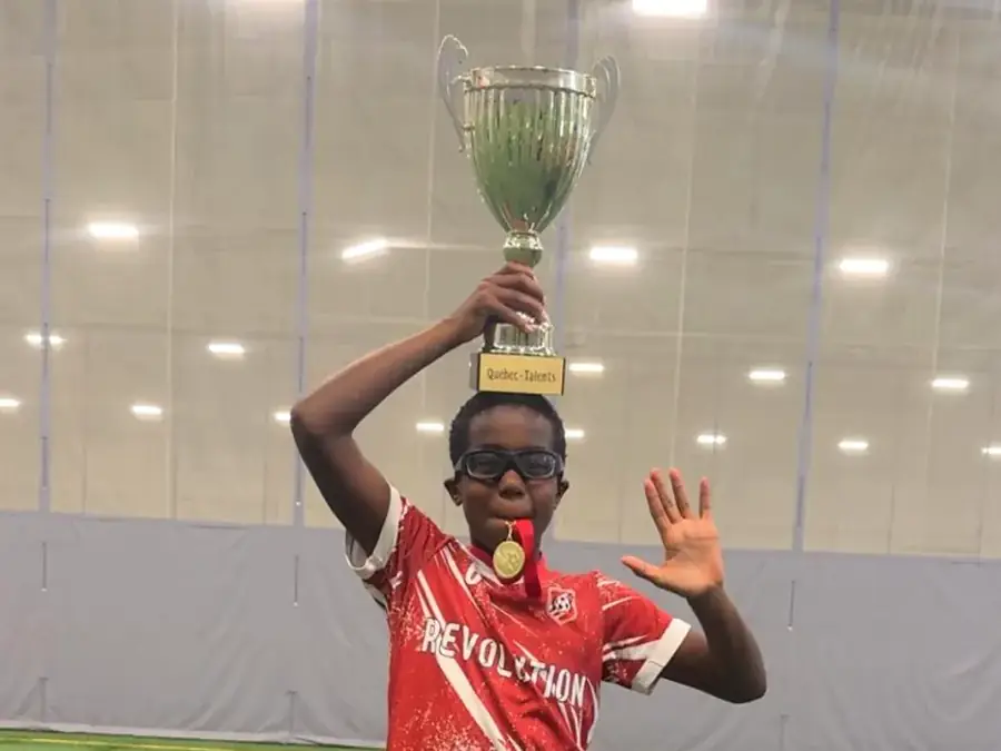 Jeune joueur Révolution brandissant la coupe au-dessus de sa tête, médaille au cou